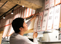 大衆酒場はんろく 求人 壁に貼るメニューは、その日の仕入れ状況により、スタッフの手で書いています。ちなみに貼っているのがオーナーです。